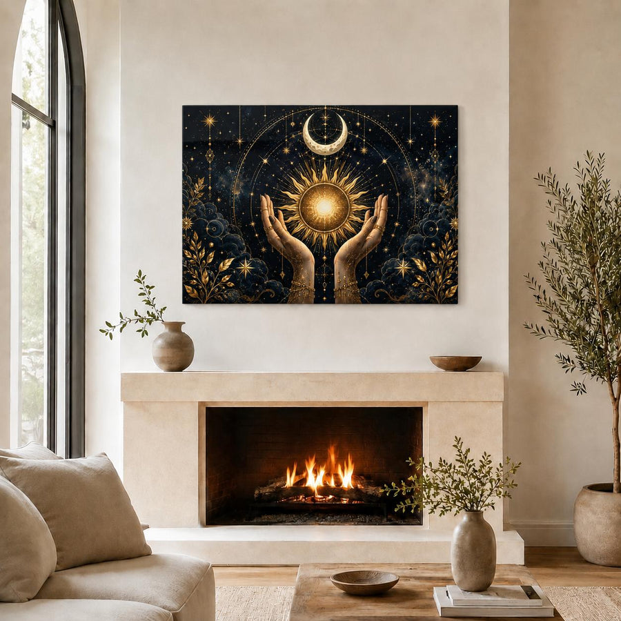 A framed wall art print depicting two hands holding a glowing sun with a crescent moon and stars, displayed above a fireplace in a styled living room with a sofa, plants, and vases.