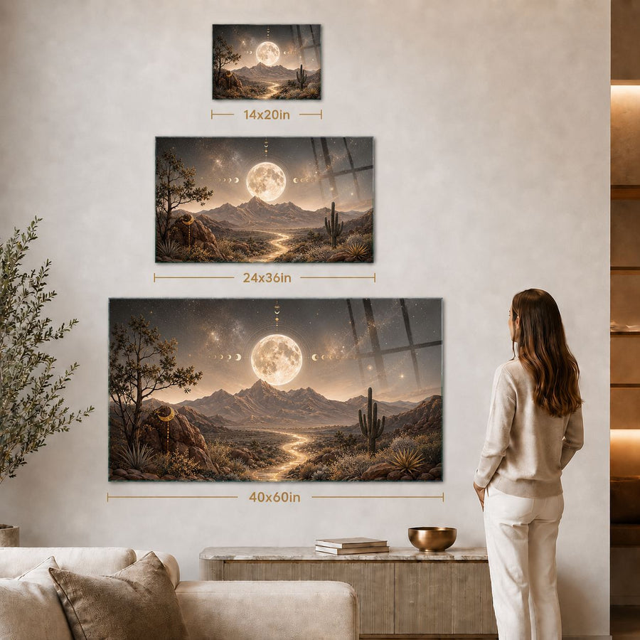 Three framed desert landscape wall art prints are displayed on a beige wall in a living room setting, with a woman standing to the right. The prints show a moonlit desert valley with mountains, cacti, and a glowing moon.