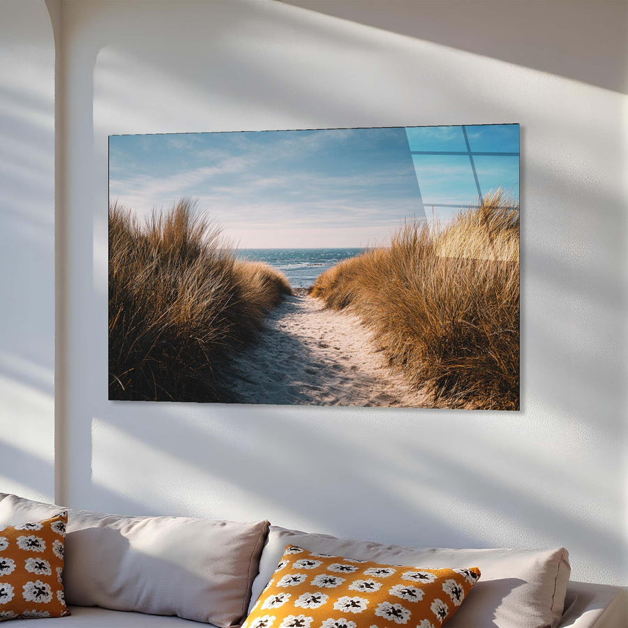 Wall art of a beach scene with sand and grass on a white wall above a sofa.
