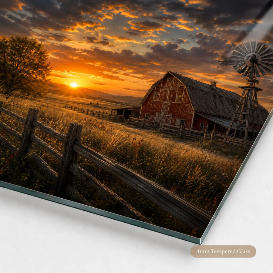A rectangular glass wall art print or panel showing a rural sunset landscape with a red barn, windmill, fence, and golden field, photographed at an angle on a white background. A small label at the bottom right reads '4mm Tempered Glass'.