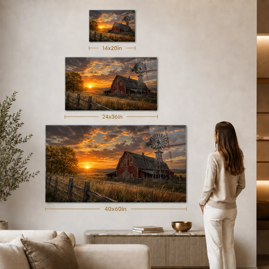 A staged interior scene showing three wall-mounted canvas prints of a sunset over a red barn and windmill, with size labels overlaid (14x20in, 24x36in, 40x60in). A woman stands to the right, looking at the largest canvas.