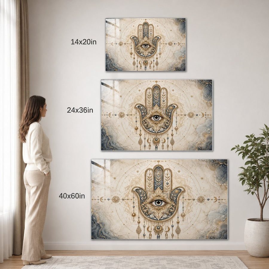 Three framed Hamsa wall art prints with overlaid size labels (14x20in, 24x36in, 40x60in) are displayed on a light wall in a styled room. A woman stands to the left, and a potted plant is on the right.